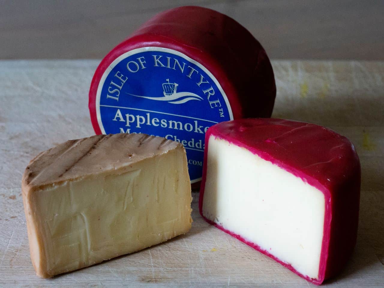 Fine Cheesemakers of Scotland: Isle of Kintyre Applewsmoke Mature Cheddar whole and cut in half on a wooden cheese board.